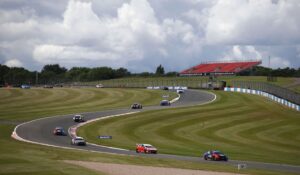 Touring cars race around a bend at Donington Park racetrack in the UK, with a red grandstand and dramatic skies in the background.