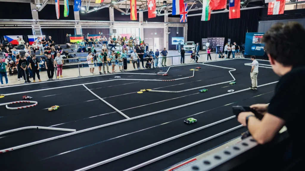 Students watch hydrogen-powered RC cars race around a black indoor track at the 2025 H2GP World Finals in Chemnitz.