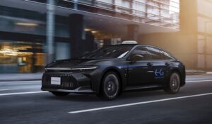 A black Toyota Crown hydrogen fuel cell taxi driving through central Tokyo with Tokyo H2 livery.