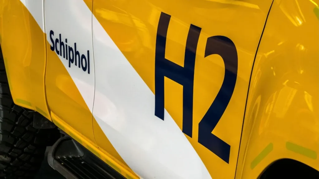 Close-up of a yellow hydrogen-powered Toyota Hilux pick-up truck marked with ‘Schiphol’ and ‘H2’ logos at Schiphol Airport.