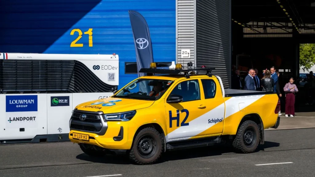 Close-up of a yellow hydrogen-powered Toyota Hilux pick-up truck marked with ‘Schiphol’ and ‘H2’ logos at Schiphol Airport.