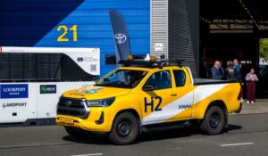 Close-up of a yellow hydrogen-powered Toyota Hilux pick-up truck marked with ‘Schiphol’ and ‘H2’ logos at Schiphol Airport.