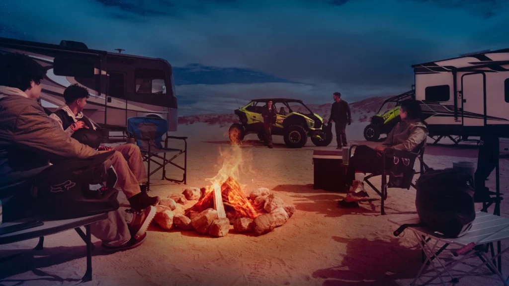 Group relaxing by campfire beside the Kawasaki Teryx H2 off-roader in desert campsite