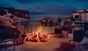 Group relaxing by campfire beside the Kawasaki Teryx H2 off-roader in desert campsite