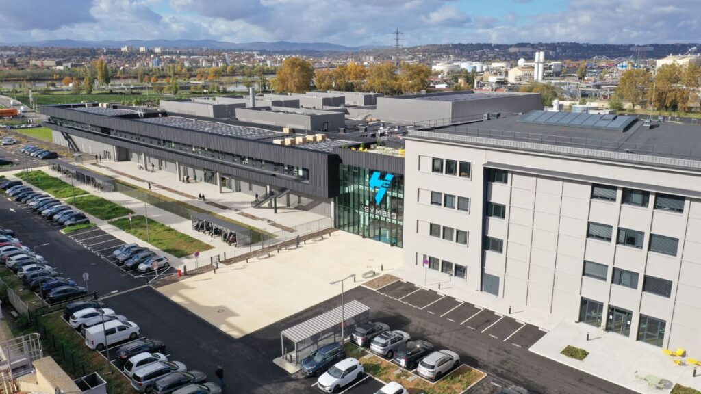 Aerial view of Symbio’s SymphonHy hydrogen fuel cell gigafactory in Saint-Fons, France, with visible solar panels, parking lots, and industrial buildings.